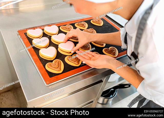 Absorbed confectioner woman using pastry bag to put cream on top of cookies