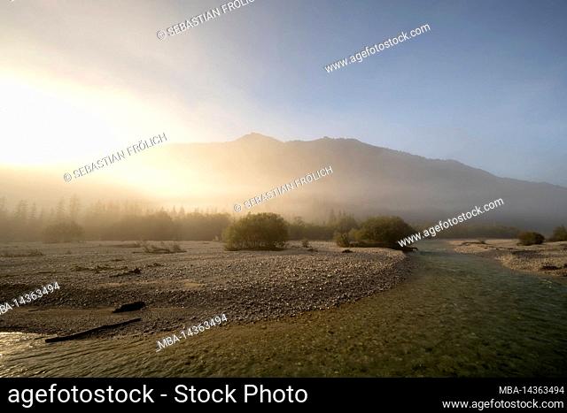 Foggy sunrise of the Isar in autumn, in the background the Karwendel mountains, in the foreground the river course with its clear water