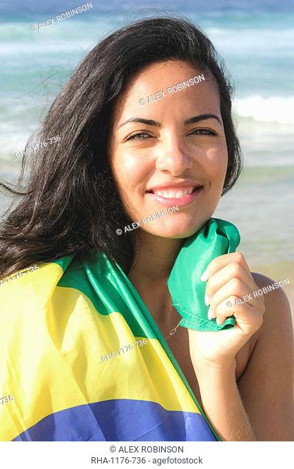 Young Brazilian woman, 20 to 29 years old, wrapped in the Brazilian flag on a beach in Rio de Janeiro, Brazil, South America