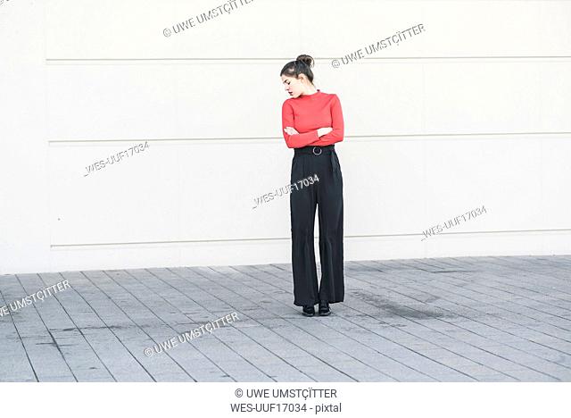 Elegant young woman standing at a wall with crossed arms