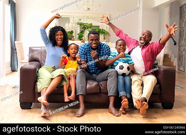 African american multi-generational family cheering while watching soccer match on tv