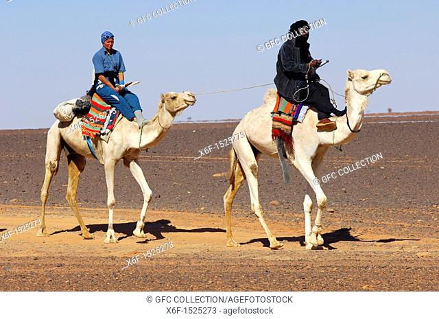 Tuareg nomad guide and an exhausted tourist on their droemdaries during a desert rode in the Sahara desert, Libya