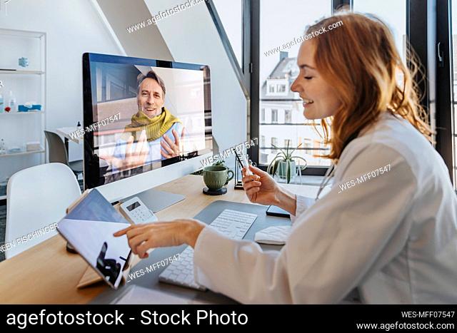 Smiling patient talking to doctor through computer while sitting at office
