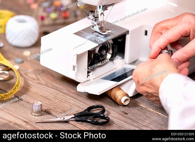 Close-up of senior woman seamstress hands removing the bobbin case in order to do the maintenance of a electrical sewing machine