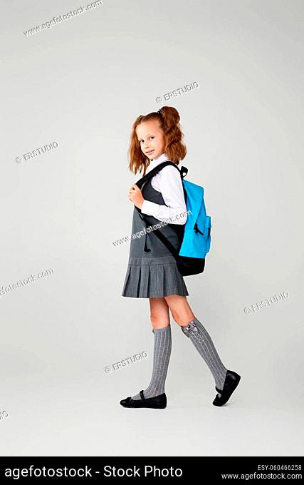 adorable schoolgirl with blue backpack isolated on gray background. Back to school