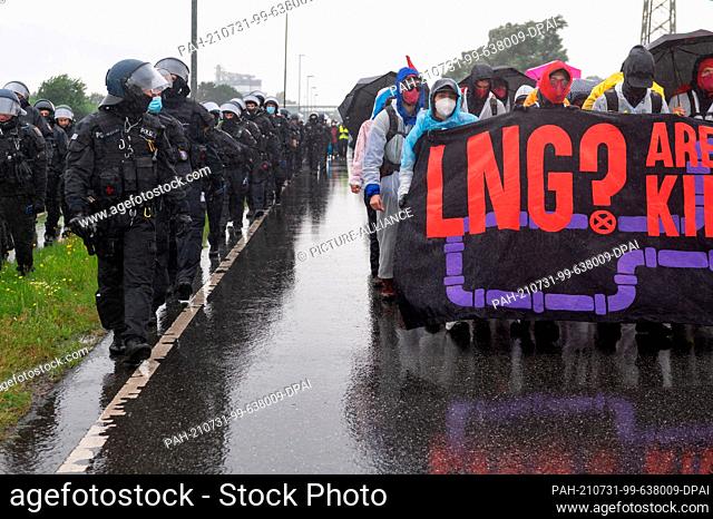 31 July 2021, Schleswig-Holstein, Brunsbüttel: Activists, accompanied by police, walk with a placard reading ""LNG? Are you fracking kidding me?!""