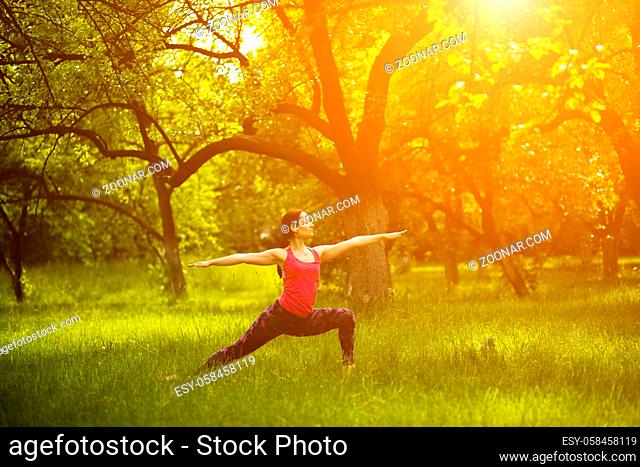 Woman practising yoga, doing Virabhadrasana 2 pose. Yoga in garden in the morning warrior 2 asana. Toned image