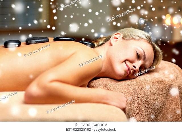 people, beauty, spa, winter and relaxation concept - close up of beautiful young woman having hot stone back massage in spa salon with snow effect