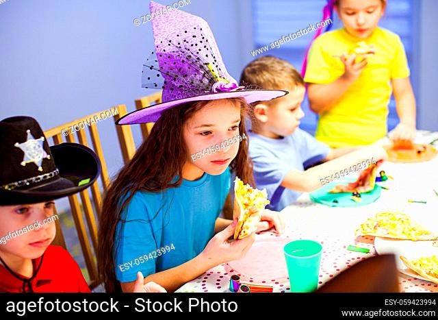 Unhappy girl eating pizza at party. Birthday celebration with pizza. Children eating pizzza at table
