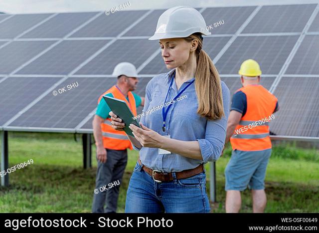 Woman using tablet PC with colleagues in background at solar station