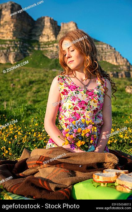 A beautiful fair-haired bride sits on a plaid plaid at the cliff with a bouquet in her hands and waits for her slob