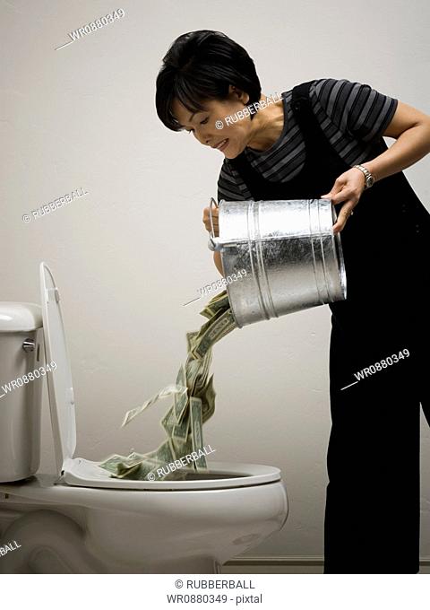 Mid adult woman emptying a bucket of money into a toilet bowl
