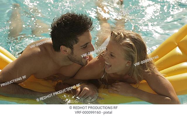 young couple playing and laughing on lilo in pool