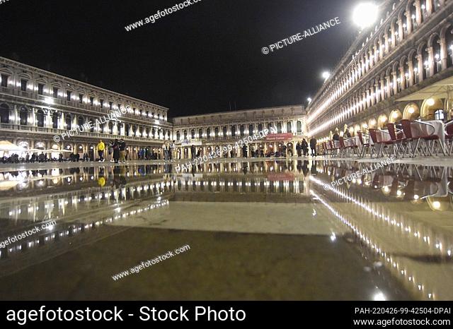 25 April 2022, Italy, Venedig: Lights are reflected in a puddle in St. Mark's Square at night while the Art Biennale is taking place in Venice