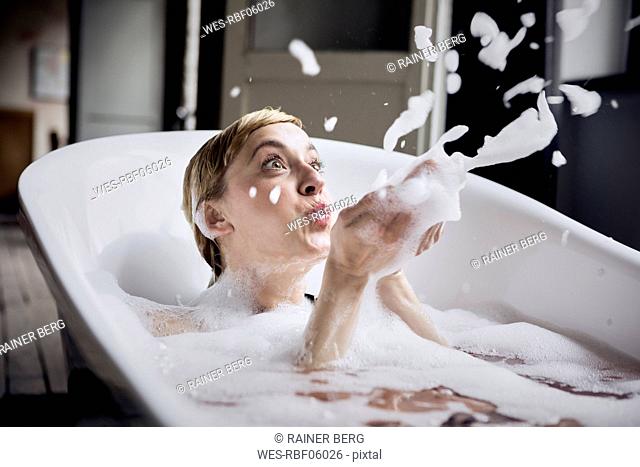 Blond woman taking bubble bath blowing foam in the air