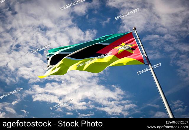 Beautiful national state flag of Mozambique fluttering at sky background. Low angle close-up Mozambique flag 3D artwork