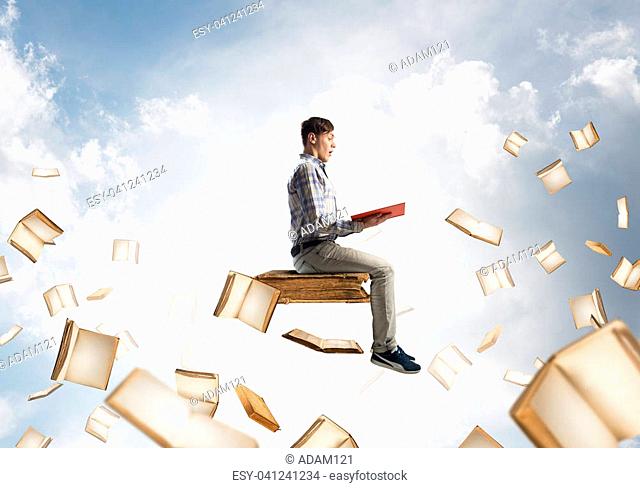Young shocked man floating in blue sky with red book in hands