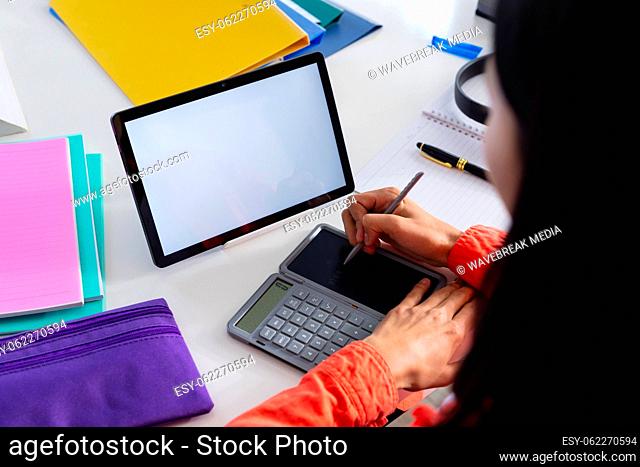 Image of biracial woman using tablet with copy space on screen and calculator sitting at desk