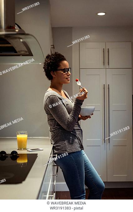 Young pregnant woman leaning on kitchen counter having food in the kitchen