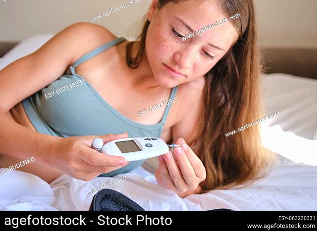 A teenage girl inserts a test strip into a glucometer to measure blood sugar. Lifestyle of a child with diabetes. Diabetes test
