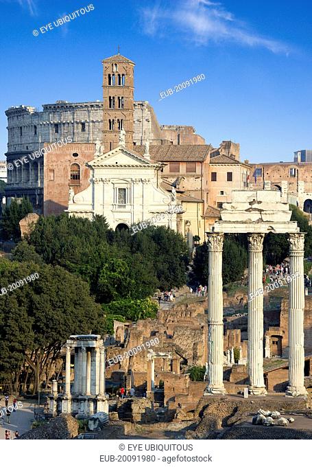 View of the Forum with the Colosseum rising behind the bell tower of the church of Santa Francesca Romana with tourists walking past the Temple of Vesta and the...