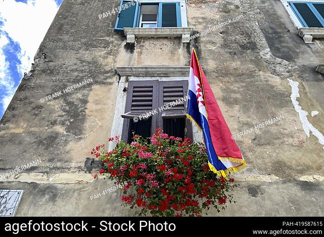 Old town of Porec / Istria in Croatia. A Croatian flag hangs on an old house facade with wooden shutters and blooming geraniums. ?