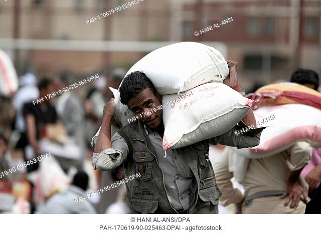 A Yemenite man carries bags of grain he has received as part of an aid donation by the government of Kuwait in Sanaa, Yemen, 19 June 2017