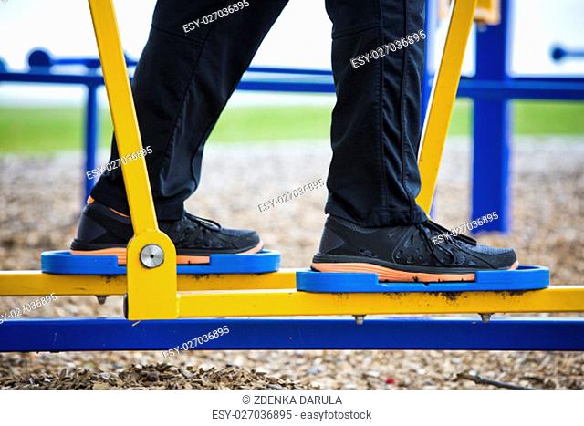 Active man in training suit exercising on elliptical trainer machine at outdoor gym