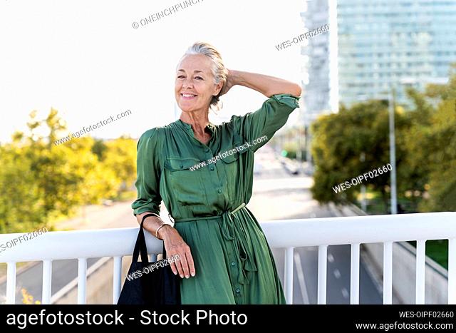 Smiling woman with hand behind head leaning on railing