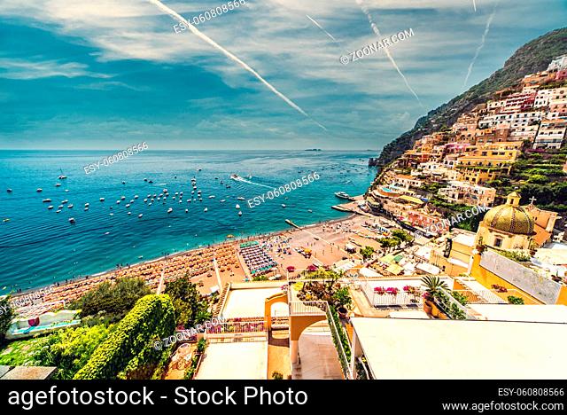 Amazing Amalfi coast with beach with parasols, hillside architecture, bright sky, view from above, jets leave white trail in cloudy sky