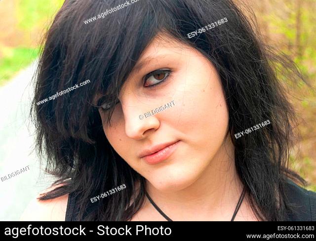 Punk emo girl, young adult with black hair and eyeliner, looking at camera, outdoors, close-up, horizontal