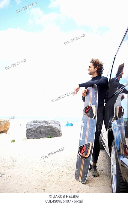 Kite surfer in wetsuit leaning against car, Hornbµk, Hovedstaden, Denmark