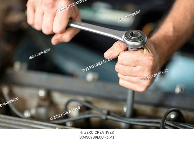 Hands of male car mechanic using wrench at repair garage