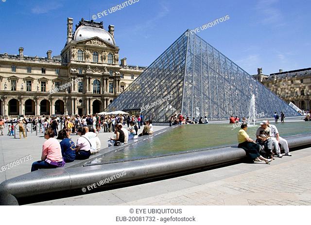 Tourists sitting beside the fountain pools in the Cour Napoleon at the Musee du Louvre with the Pyramid Entrance designed by I M Pei and the Richelieu Pavilion...