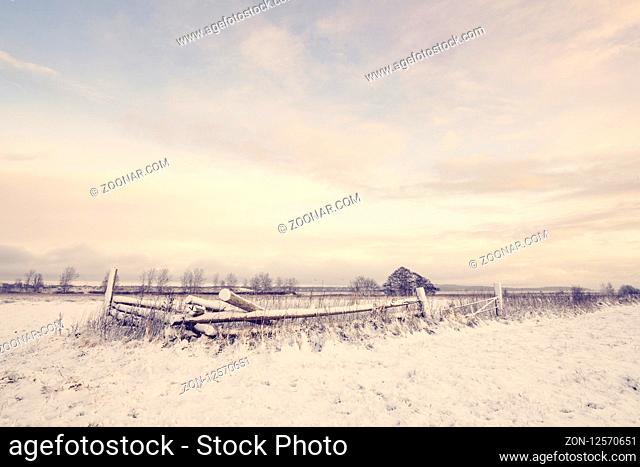 Winter scenery with a wooden fence covered in snow on a rural field in the morning sunrise