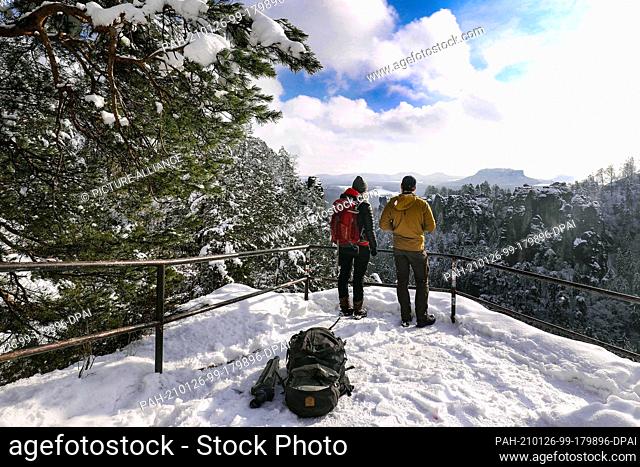 25 January 2021, Saxony, Lohmen: A woman and a man look from the pavilion view of the Bastei on the snowy Elbsandsteingebirge