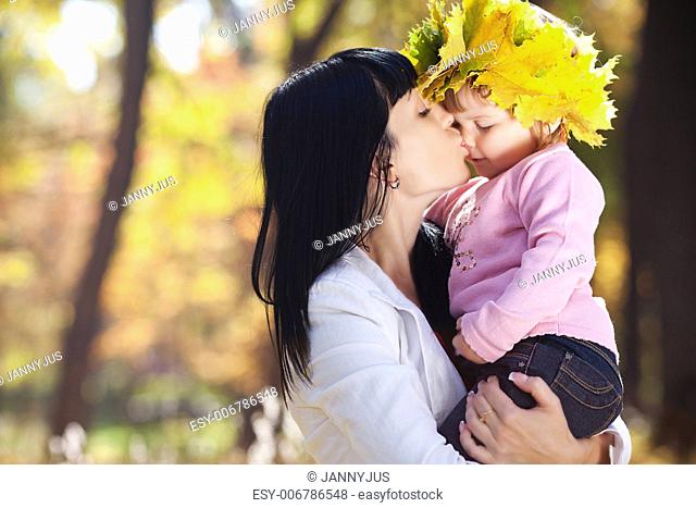 beautiful young mother kissing her daughter in autumn forest
