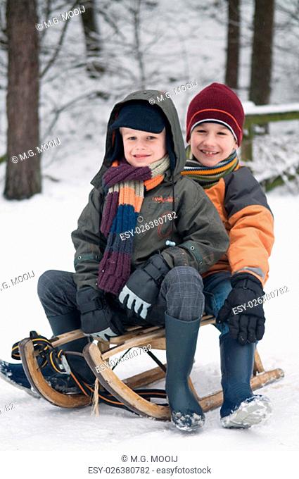 Two young boys sitting on a sled in the snow