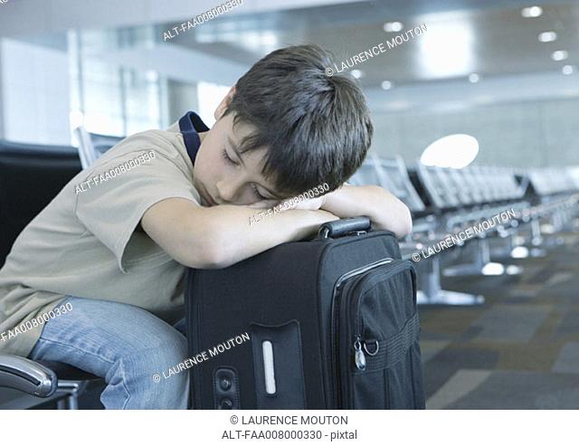 In airport lounge, boy resting head on suitcase, sleeping