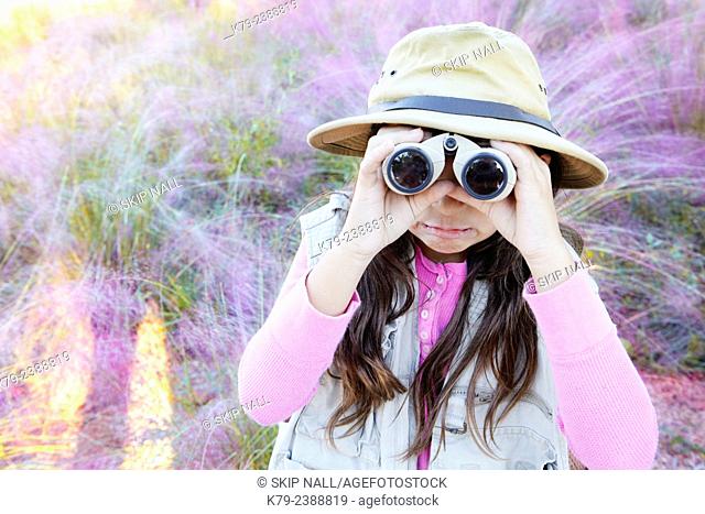 A young girl pretending to be on safari looking through binoculars