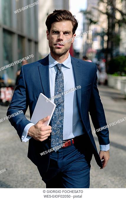 Handsome businessman walking in Manhattan, carrying digital tablet