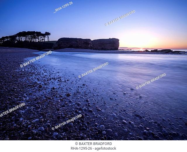 Sunrise behind the silhouetted cliff of Otter Head, where the River Otter meets the sea at Budleigh Salterton, Devon, England, United Kingdom, Europe