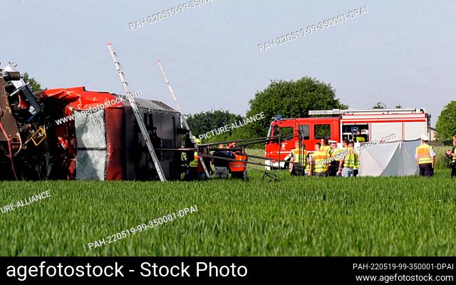 19 May 2022, Hessen, Münster: A locomotive lies next to the tracks in a field, firefighters and police stand next to it. A train driver has died in an accident...