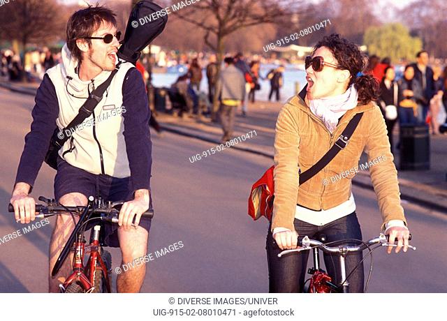 A man and woman, on bicycles, riding through a park, London, UK 2004