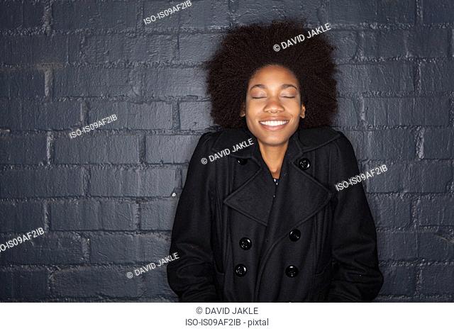 Young woman by black brick wall wearing black jacket