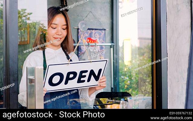Happy Asian beautiful young woman staff turning round sign to open on door, Female owner of coffee shop opening the service after lockdown quarantine