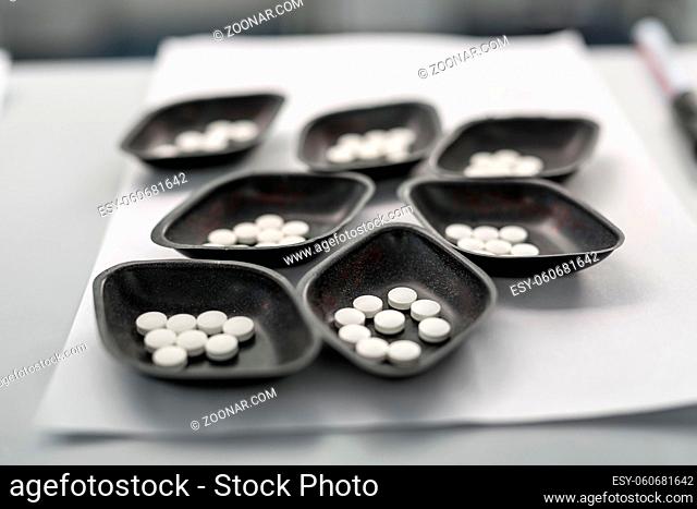 Several small dark bowls with white placebo pills on the light surface on the blurry background. Closeup. Horizontal