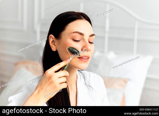 Beautiful european woman uses jade roller to massage her face. Spa self beauty procedure
