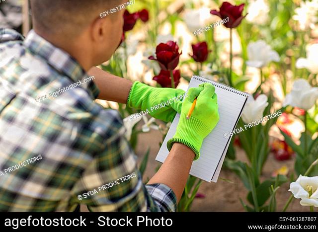 man with notebook and flowers at summer garden