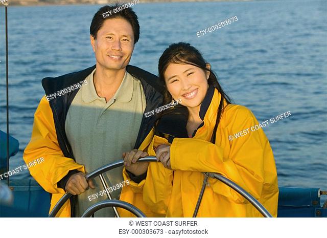Couple wearing yellow anoraks at steering wheel of sailboat portrait